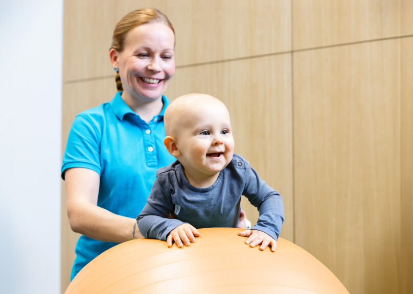 Vauva jumppapallon päällä naisterapeutin tukemana