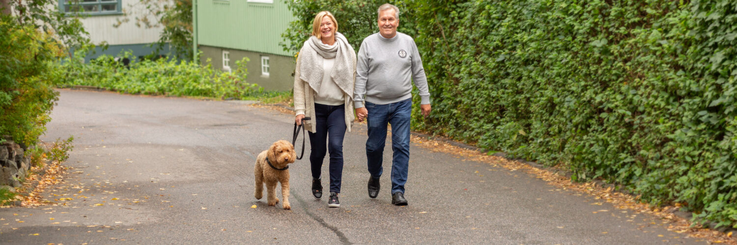 Keski-iän ylittänyt pariskunta kävelemässä koiran kanssa puutaloalueella