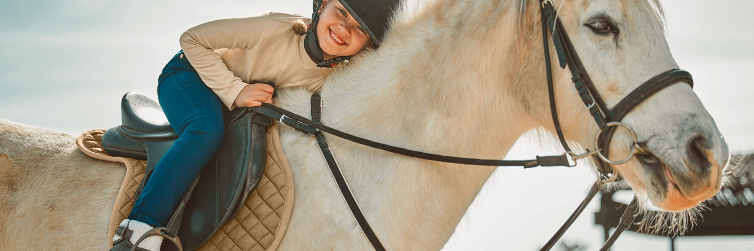 Hymyilevä tyttö istuu hevosen selässä ja halaa hevosta.