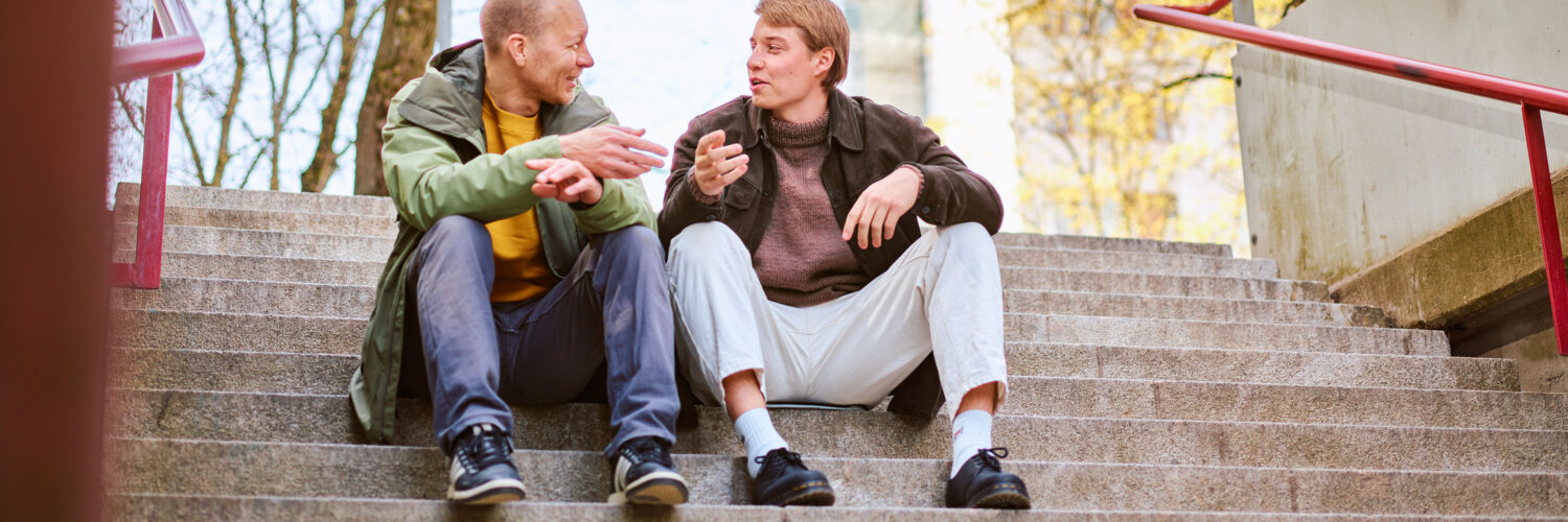 mies ja nuori mies keskustelevat ulkona portailla